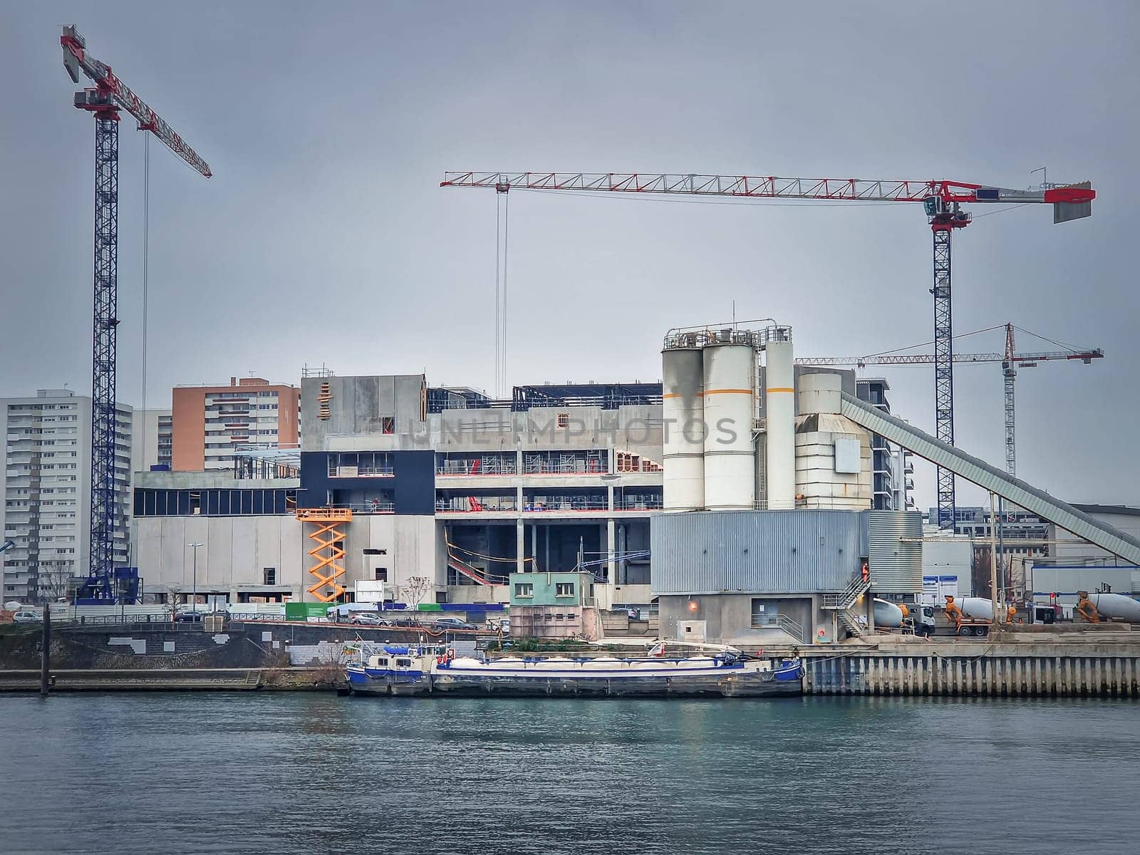 Busy building site near Seine river with cranes working and a barge on the water, Asnieres, Paris, France