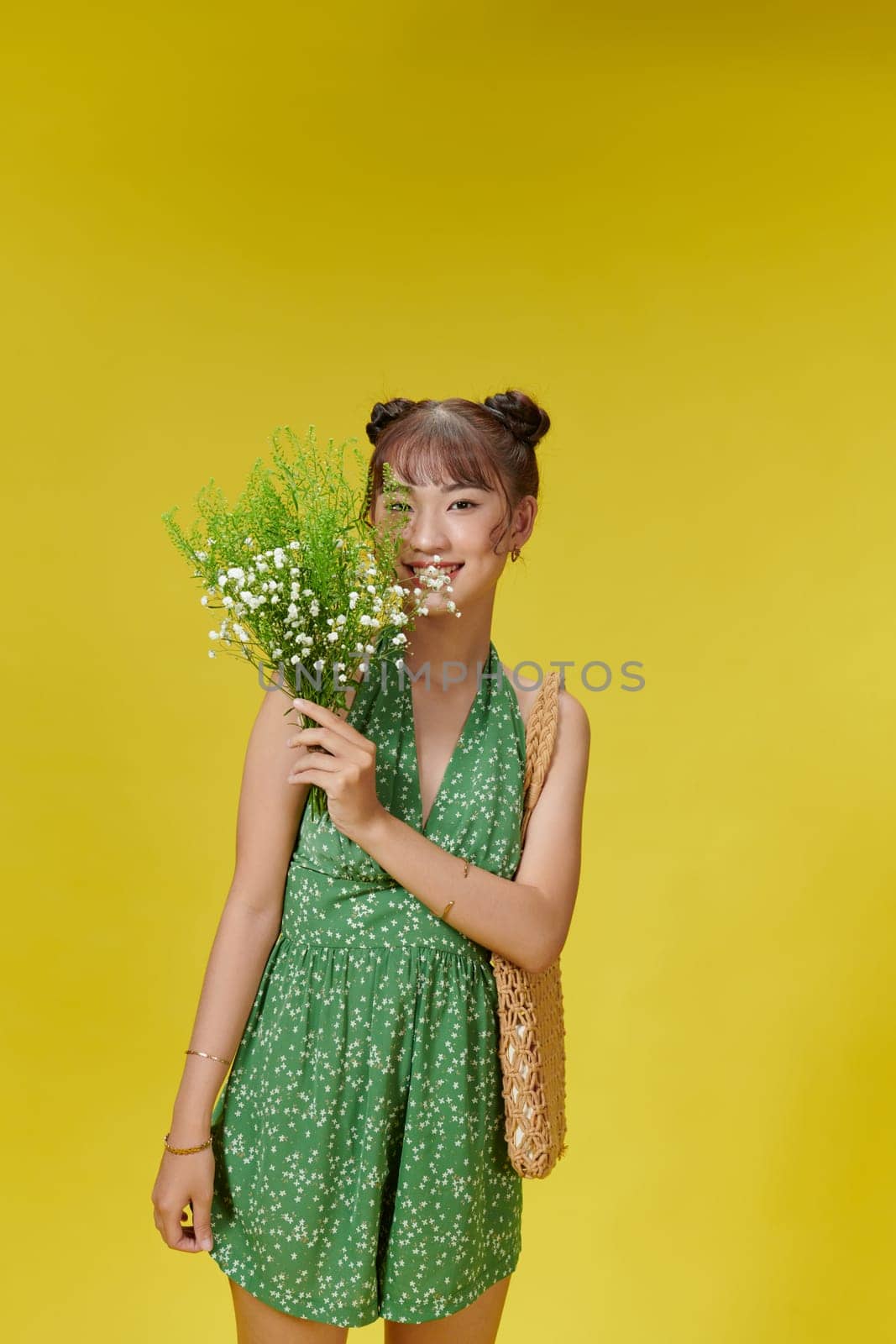 Charming asian woman in green summer jumpsuit with wildflowers in her hands smiling by makidotvn