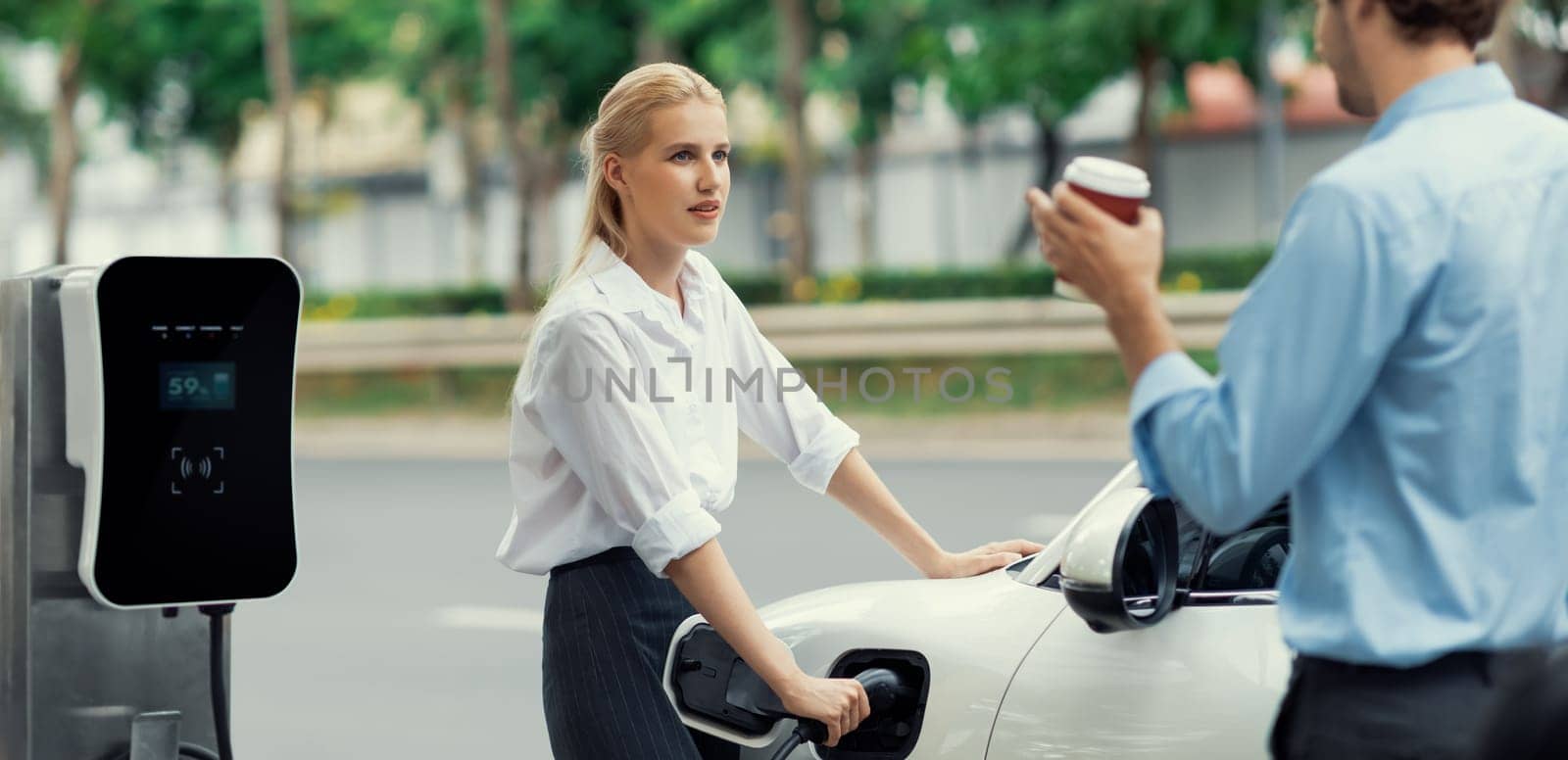 Progressive businessman and businesswoman at charging point and EV car by biancoblue