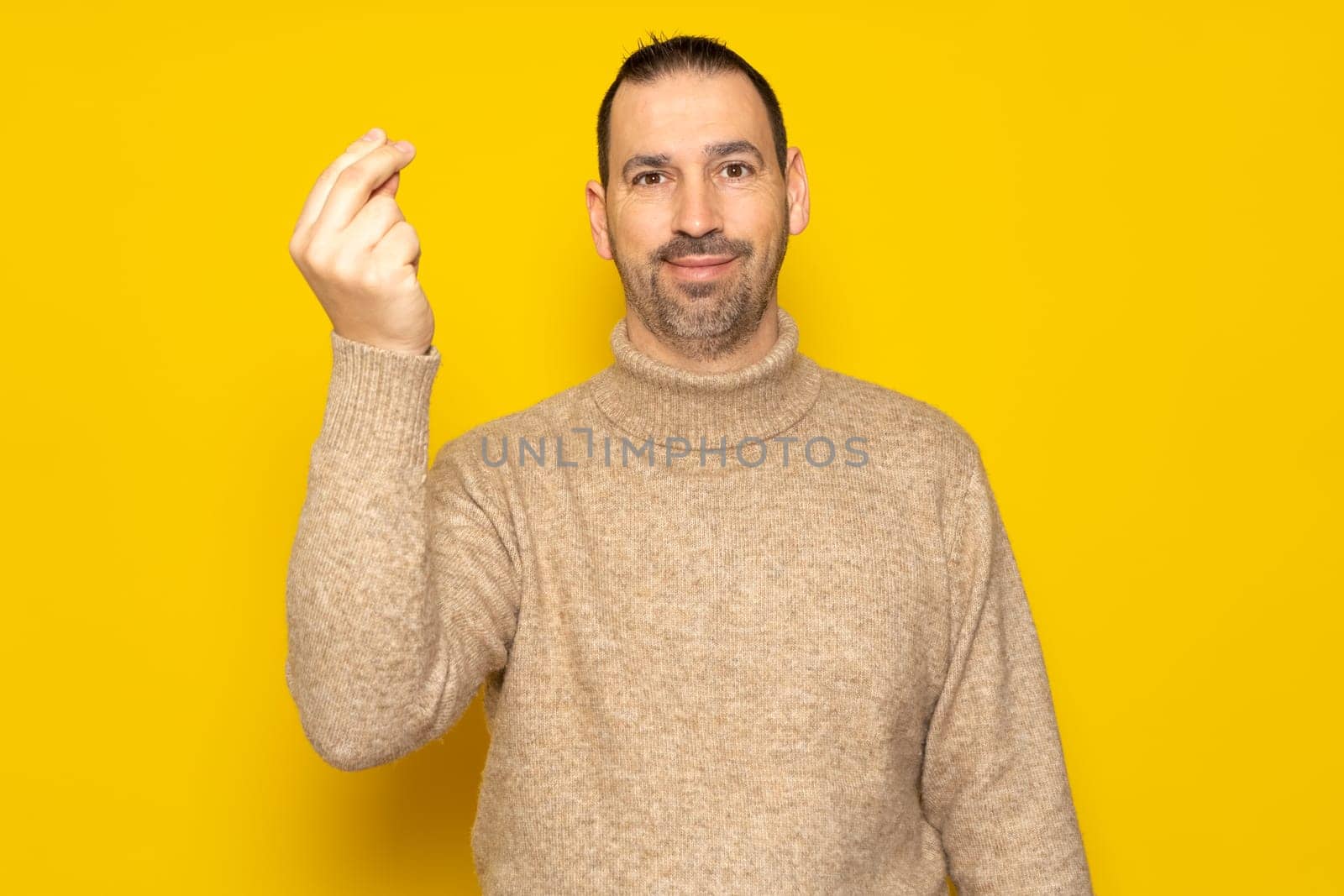 Bearded Hispanic man wearing a beige turtleneck making an Italian mama mia gesture while smiling at the camera, isolated over yellow background.