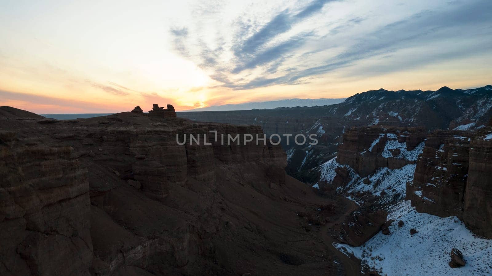 Charyn Grand Canyon with orange rock walls. Aerial view from the drone of the steep canyon walls, cracks and tunnels. There is snow in places. Beautiful sunset and sunrise. Brother of the Grand Canyon