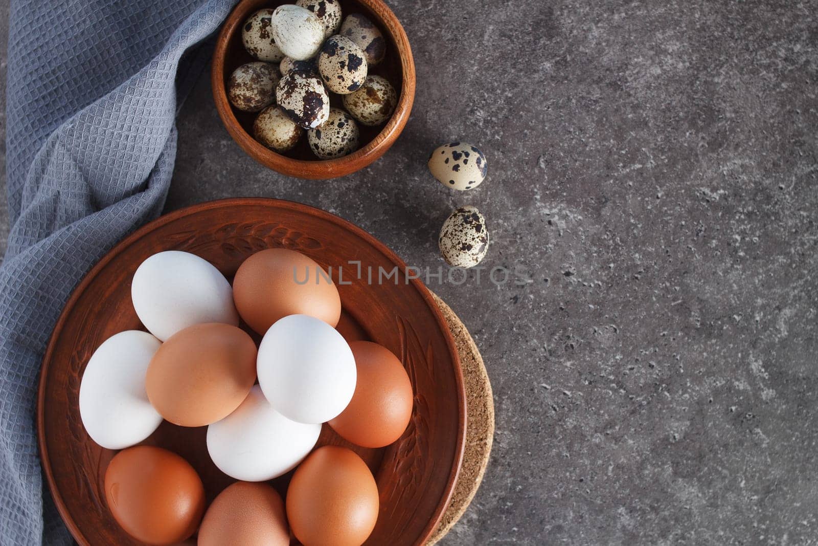 Chicken and quail eggs on a plate on a concrete background with textiles. copy space