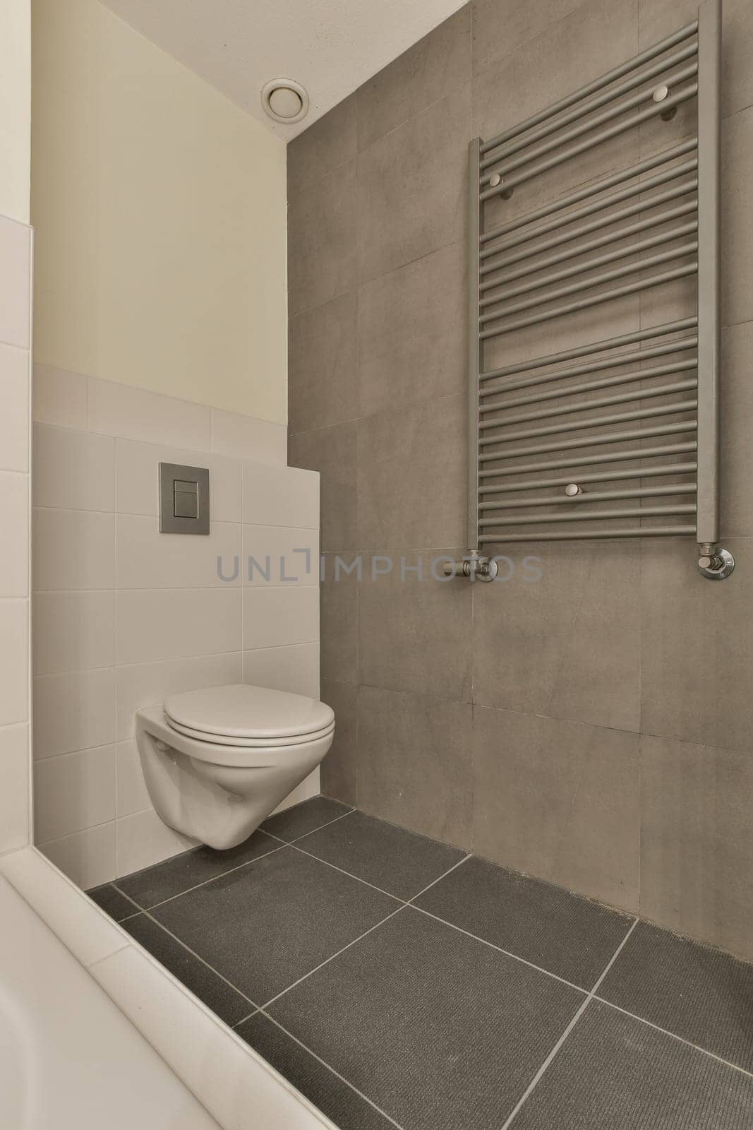 a bathroom with a white toilet and gray tiles on the floor in front of the bathtub, which is attached to the wall