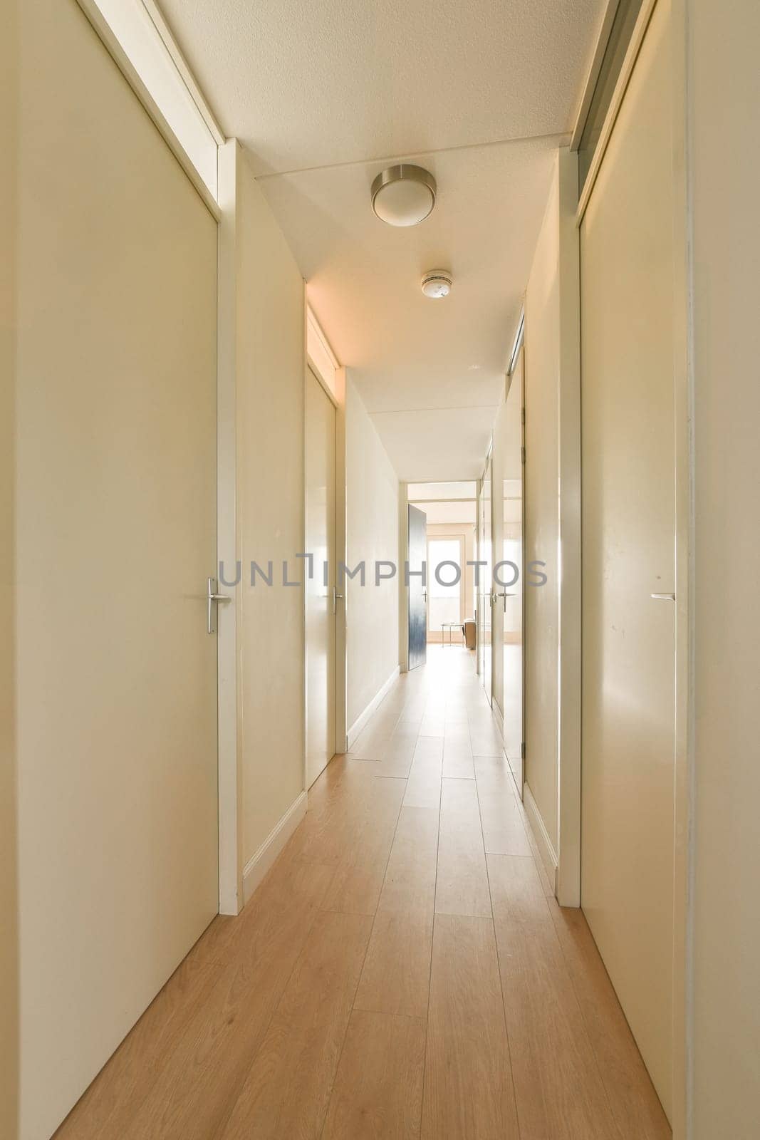 a long hallway with white walls and wood flooring on both sides, leading to an open door that leads to another room