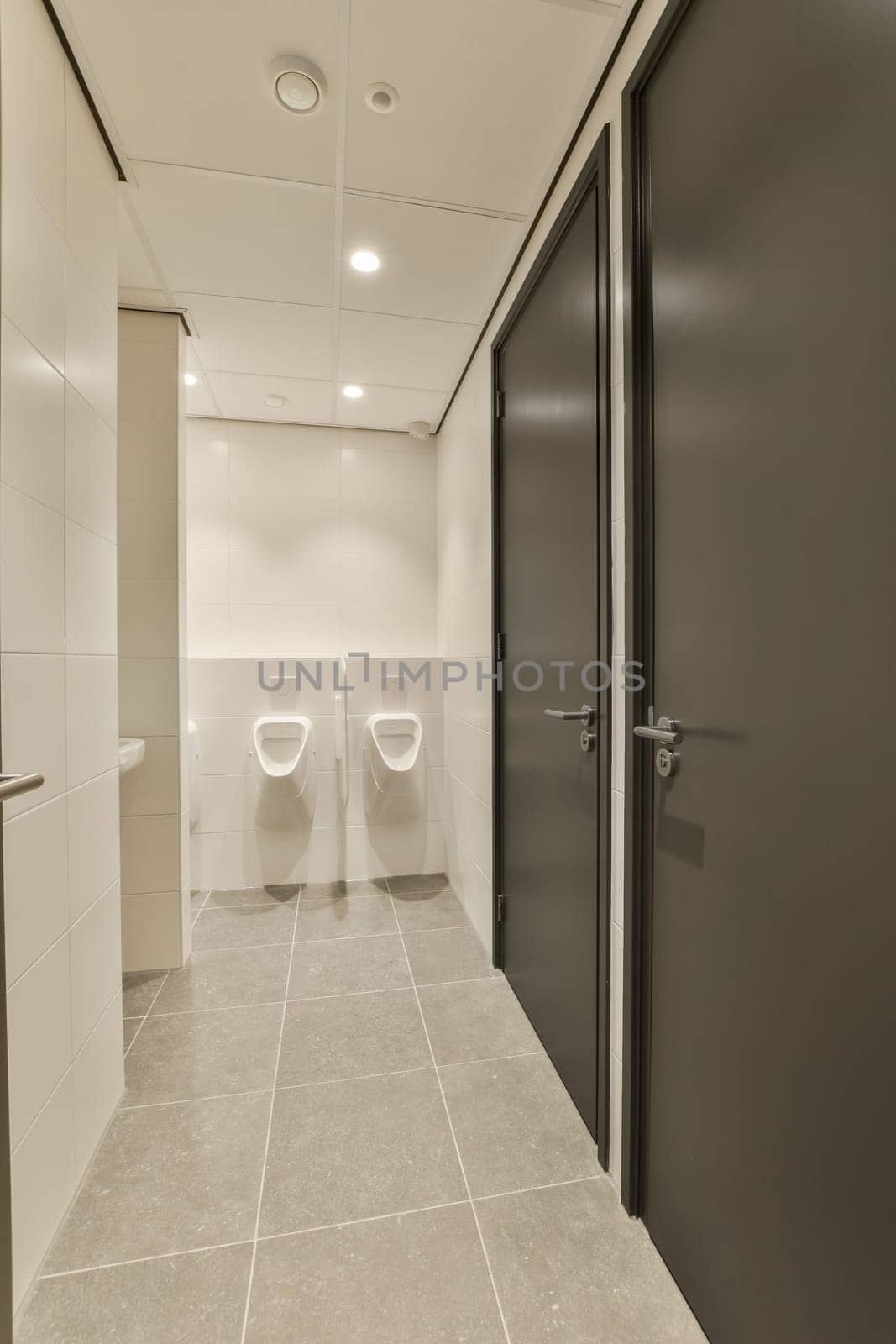 a bathroom with two urinals and a black door by casamedia