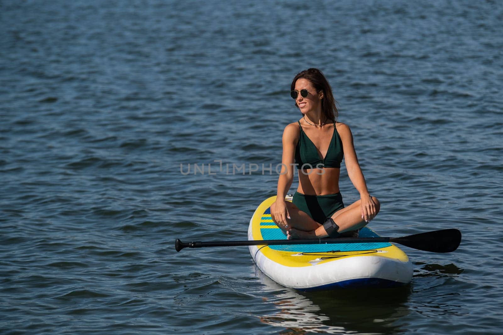 Caucasian woman sitting in lotus position on SUP board on the lake. Summer sports