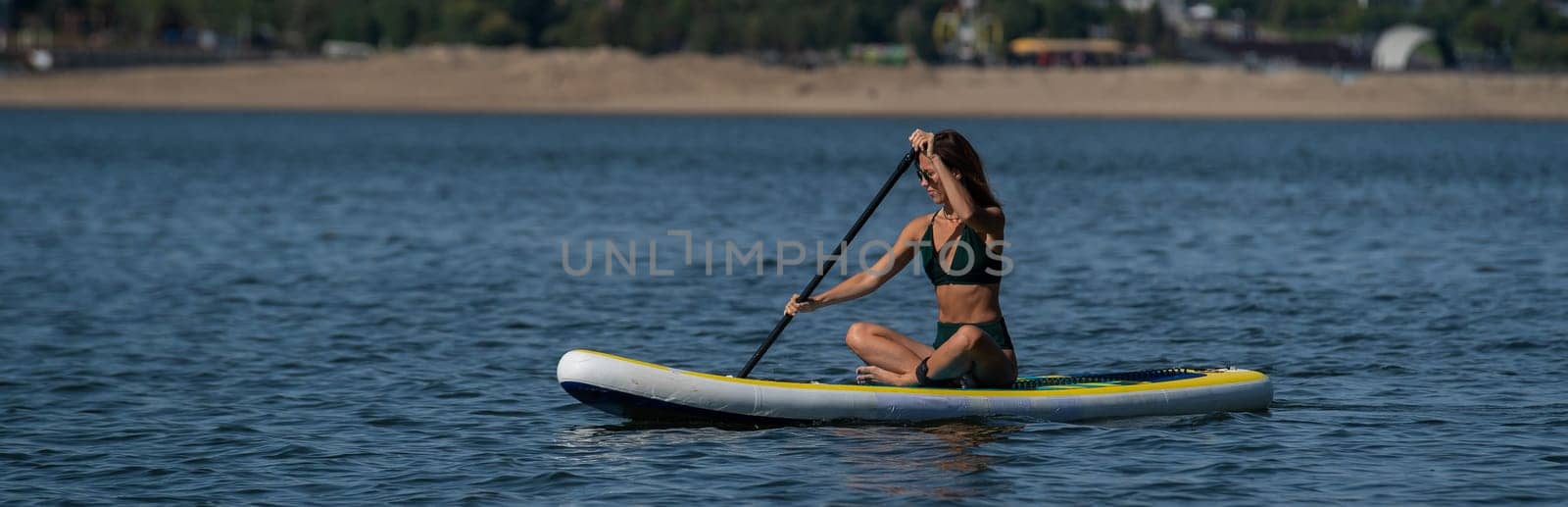 Caucasian woman is riding a SUP board on the river in the city. Summer sport