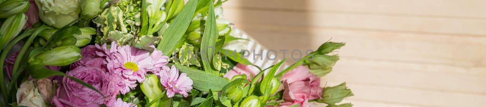 two bouquets of roses, daisies, lisianthus, chrysanthemums, unopened buds on a plank table and a background of pink silk fabric with pleats.