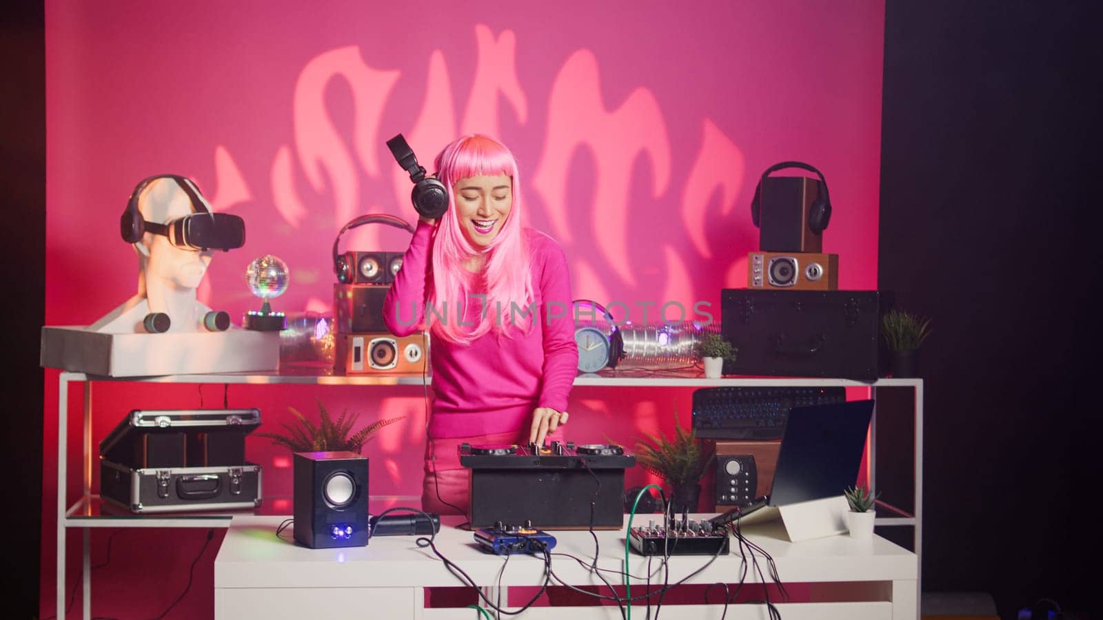 Artist standing at dj table performing electronic song using professional mixer console, enjoying playing music during night time in club. Perfomer with pink hair doing performance with audio equipment