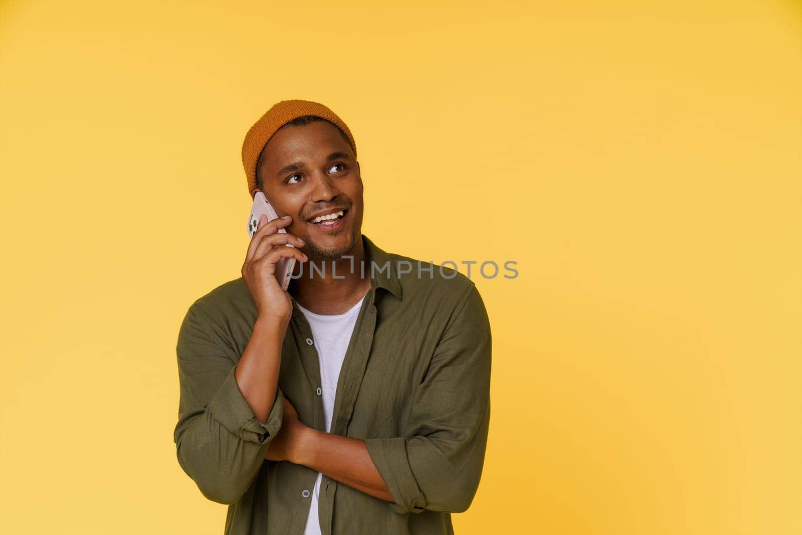Smiling African man wearing orange cap is having phone call, with copy space on yellow background. Perfect for product placement and advertising concepts. High quality photo