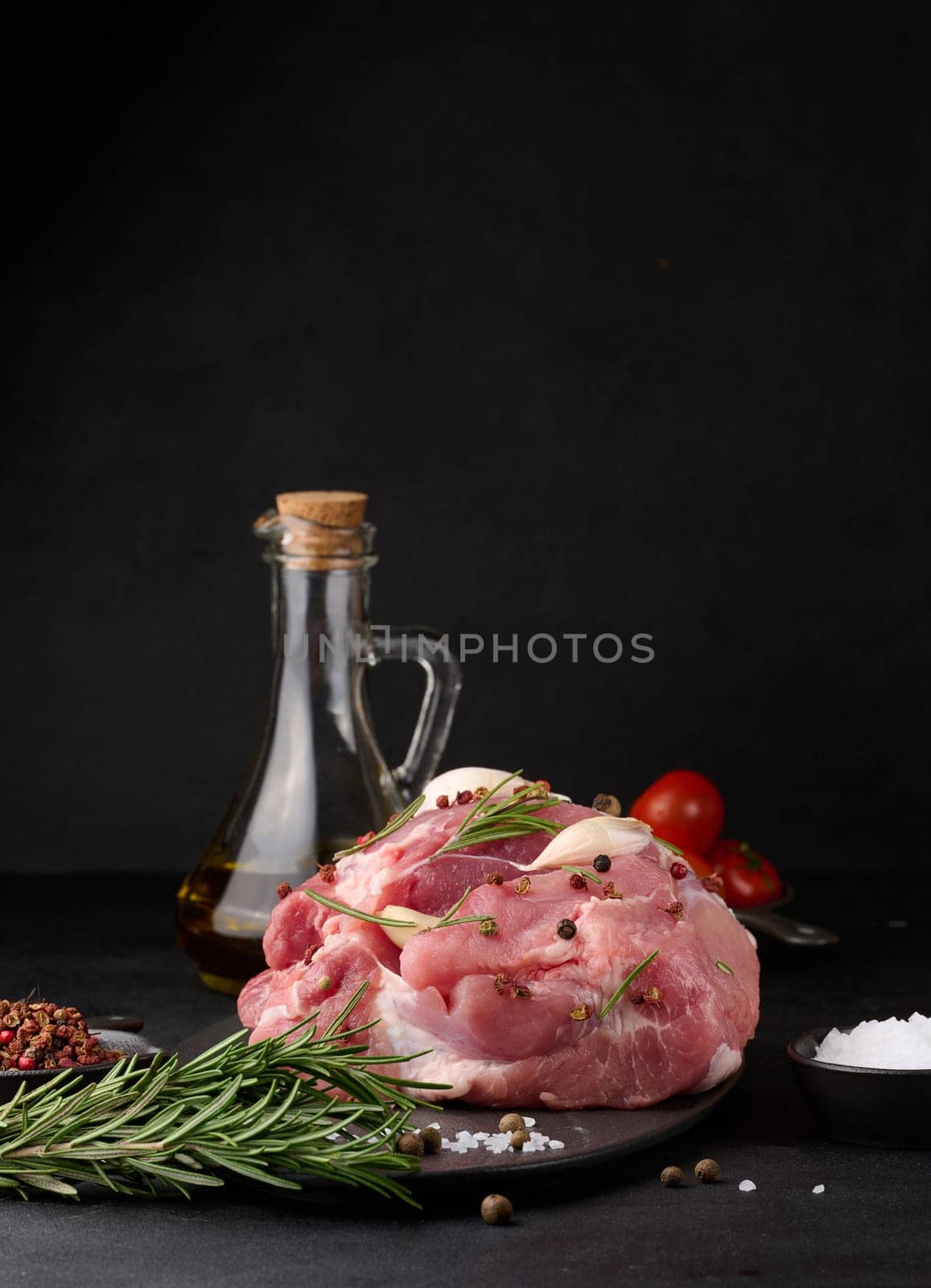 A piece of pork ham on a black board and spices olive oil, salt, rosemary branch and pepper