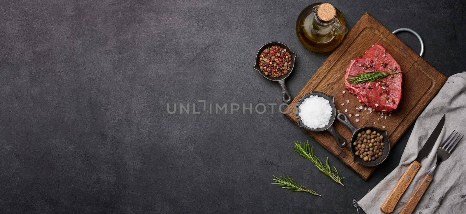 Raw piece of beef with spices pepper, rosemary sprig, salt and olive oil on a wooden board, black background. Copy space
