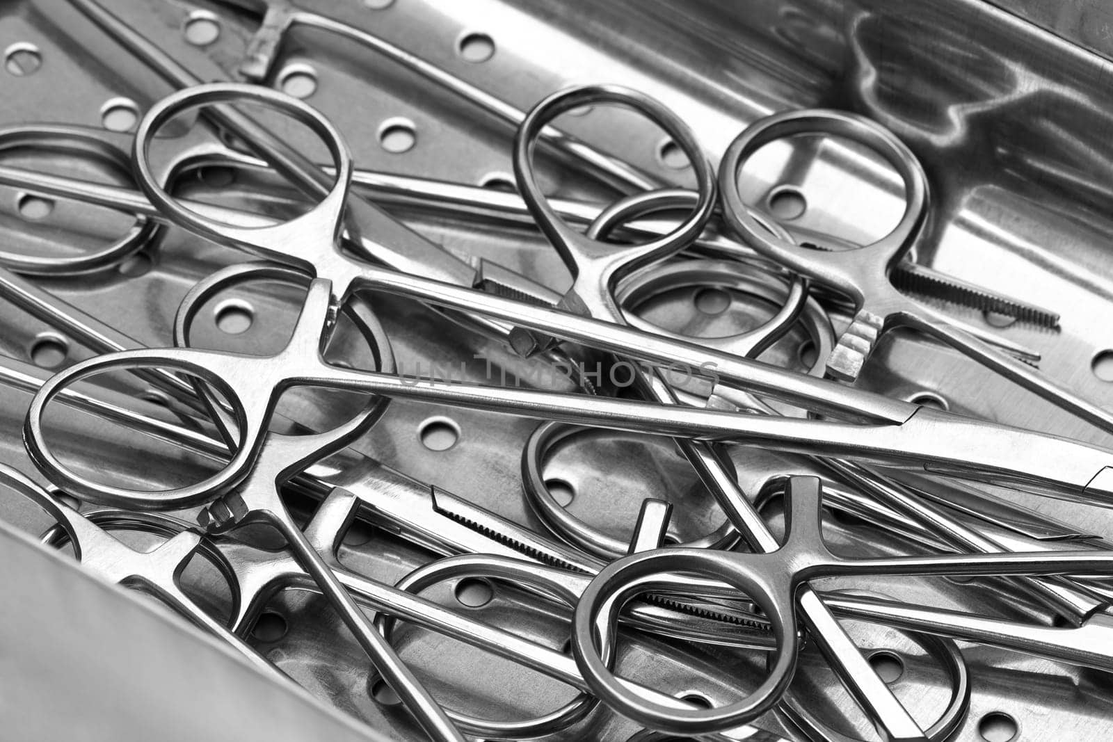 Closeup view stainless surgical needle drivers lying down on steel sterilization tray medical tools by Alexander-Piragis