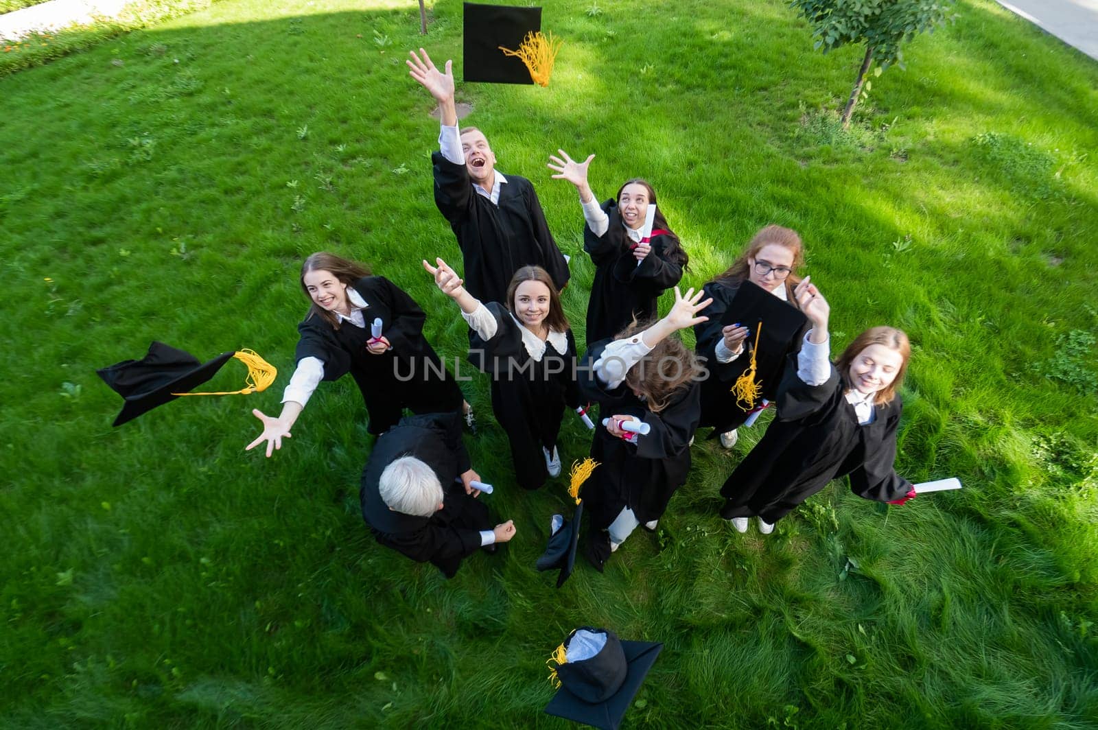 Classmates in graduation gowns throw their caps. View from above