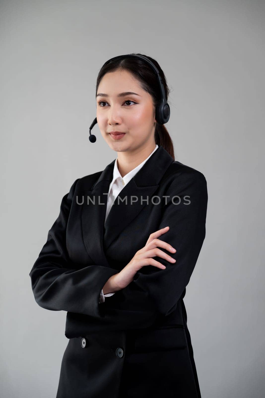 Attractive asian female call center operator with happy smile face advertises job opportunity on empty space, wearing a formal suit and headset on customizable isolated background. Enthusiastic