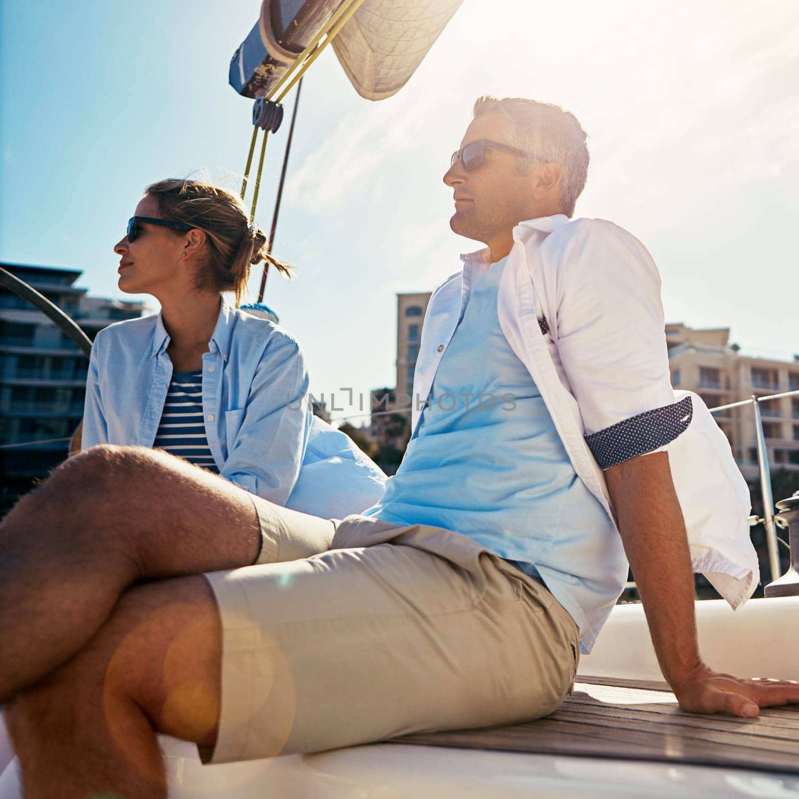 Watching the sun meet the sea. a couple out sailing on a yacht. by YuriArcurs