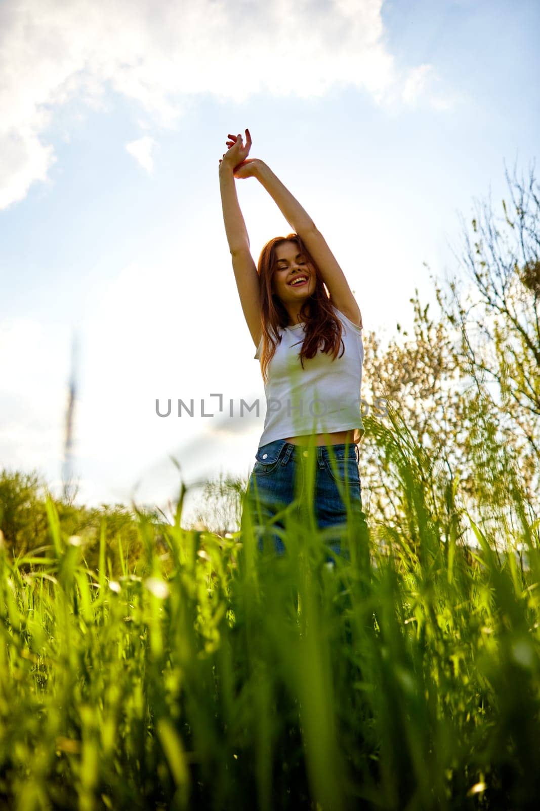 joyful slender woman posing in a field with her arms raised high. High quality photo