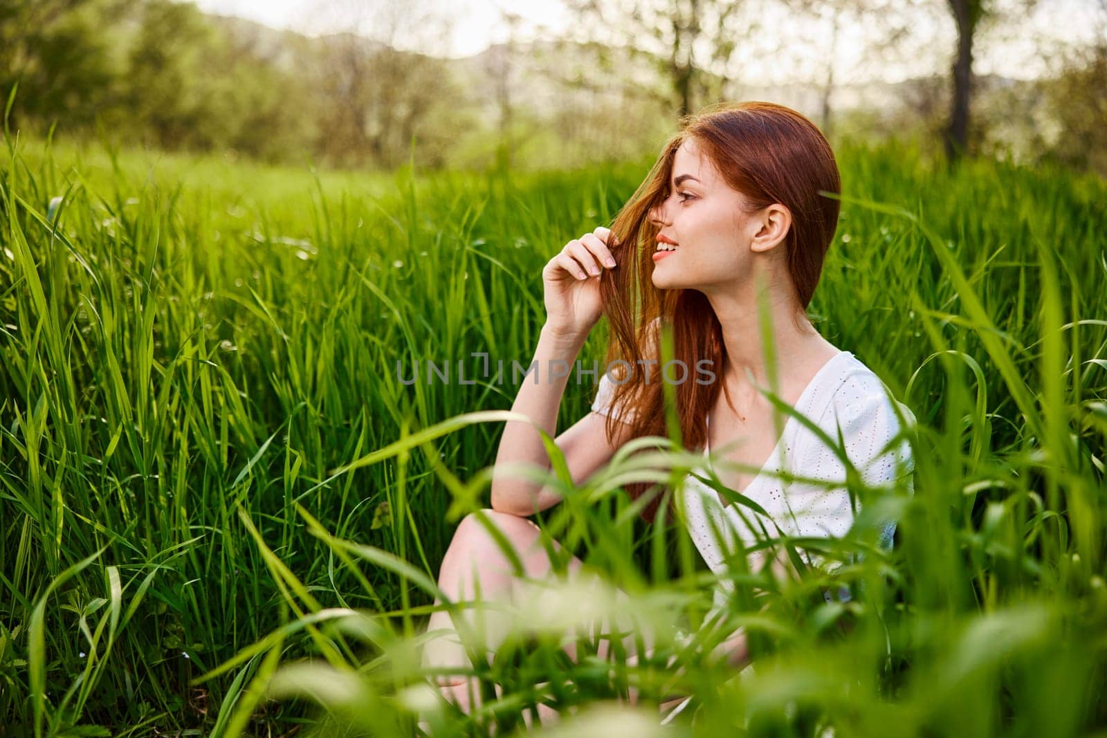 a young woman sitting resting in the tall grass straightening her hair. High quality photo