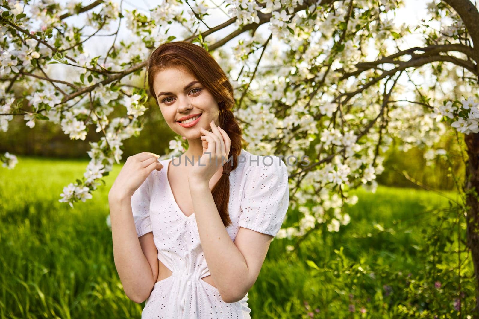 portrait of beautiful young woman standing near the apple tree on a warm summer sunny day against sun light sky background Copy space for inscription by Vichizh