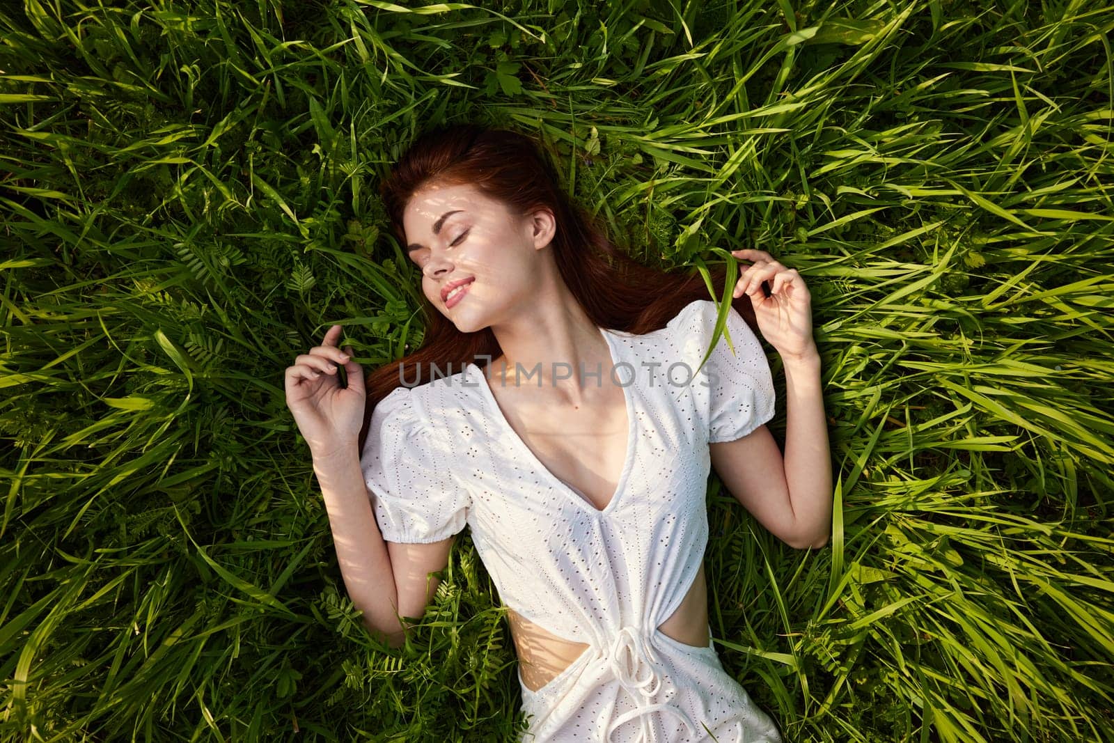 a beautiful woman with red hair lies on the grass in a white dress enjoying the day. High quality photo