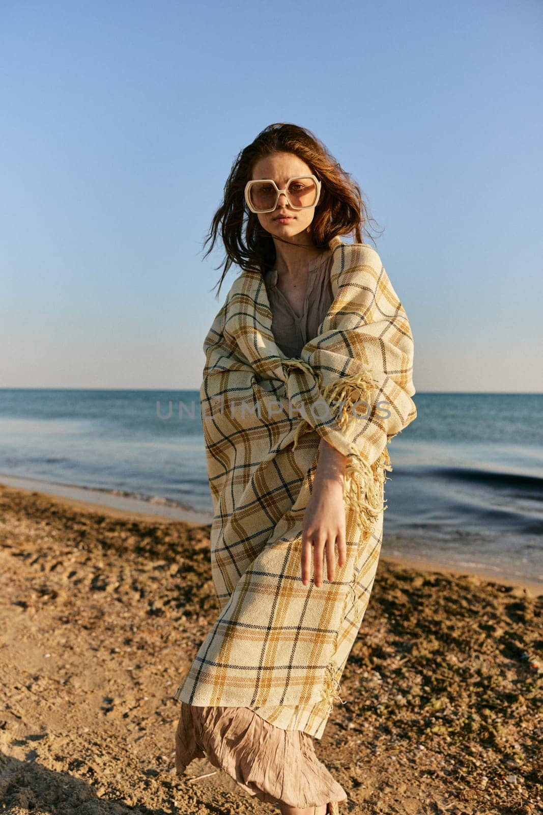 a woman wrapped in a plaid stands on the seashore in bright sunglasses. High quality photo