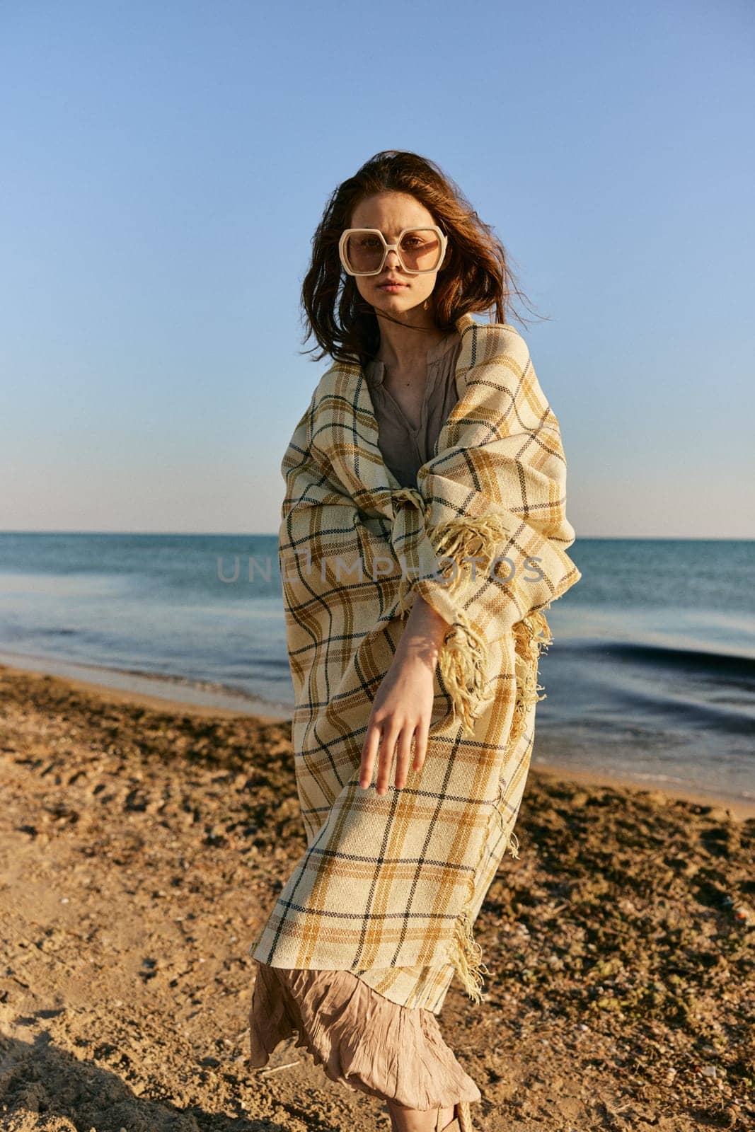 a woman wrapped in a plaid stands on the seashore in bright sunglasses. High quality photo