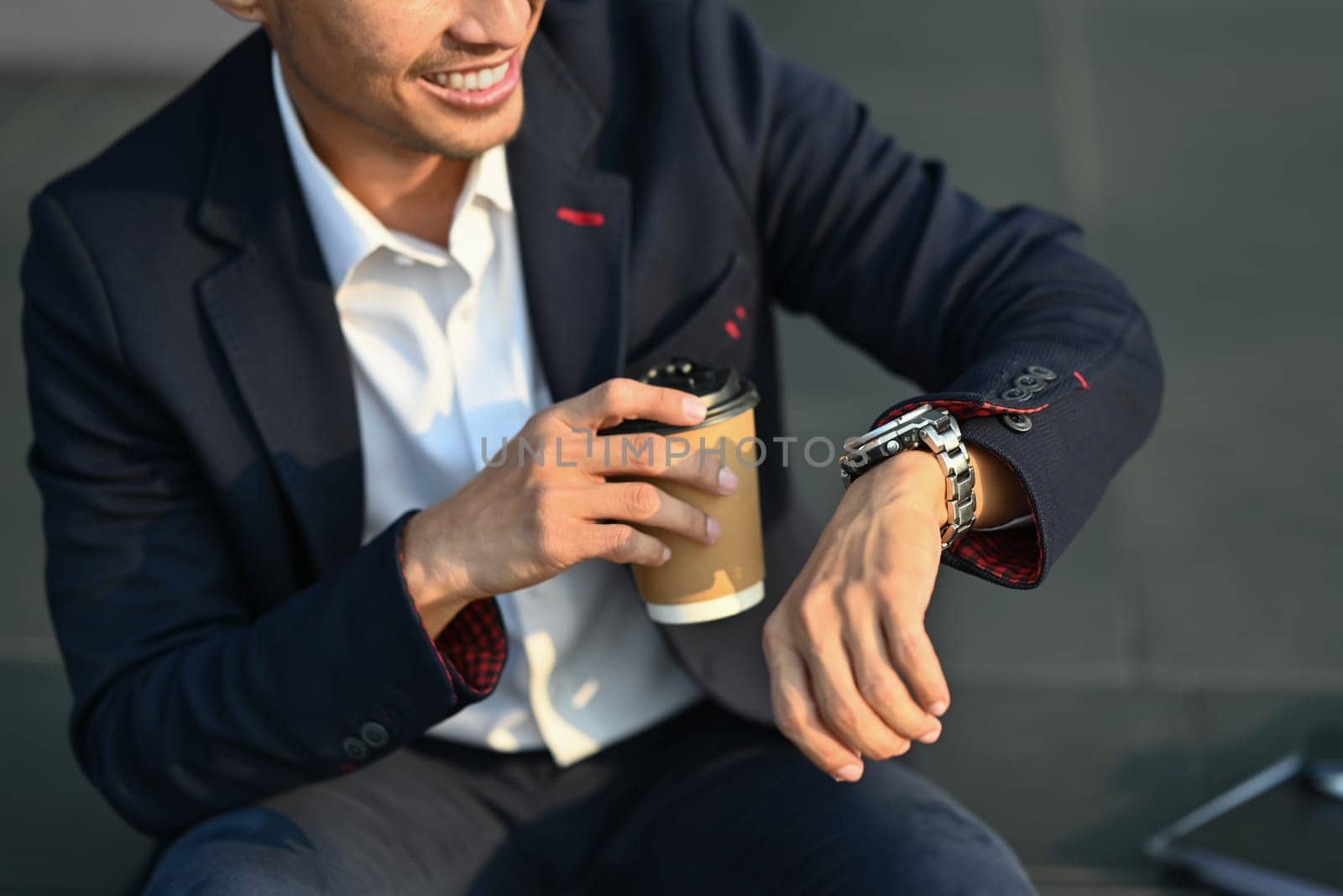 Young businessman holding takeaway coffee cup and checking time looks at wristwatch.