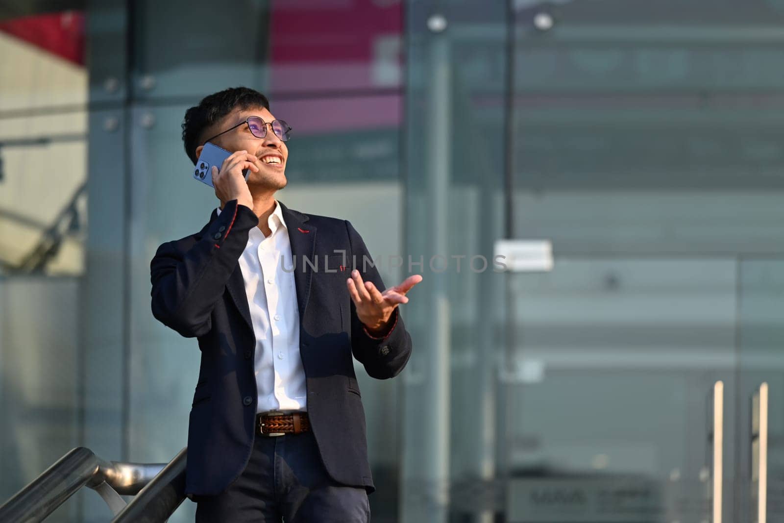 Portrait of handsome businessman wearing elegant suit talking on mobile phone at outdoors in urban modern city.