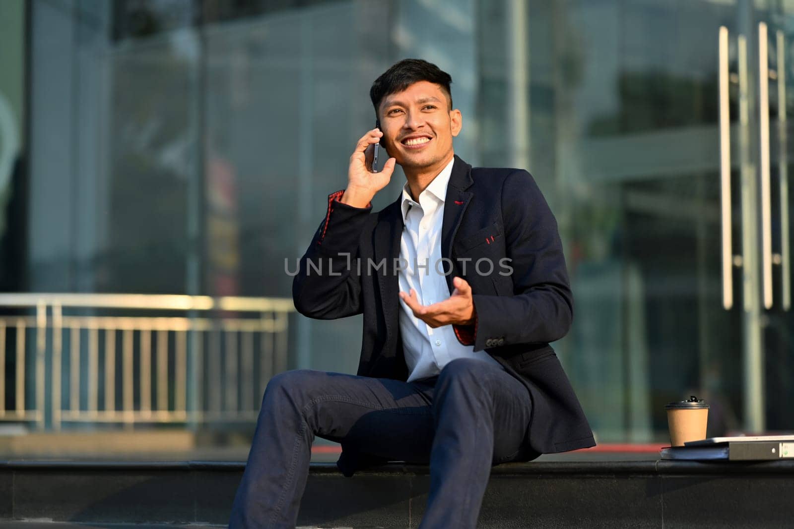 Handsome young businesswoman in formal clothes talking on mobile phone on stairs outside office building.