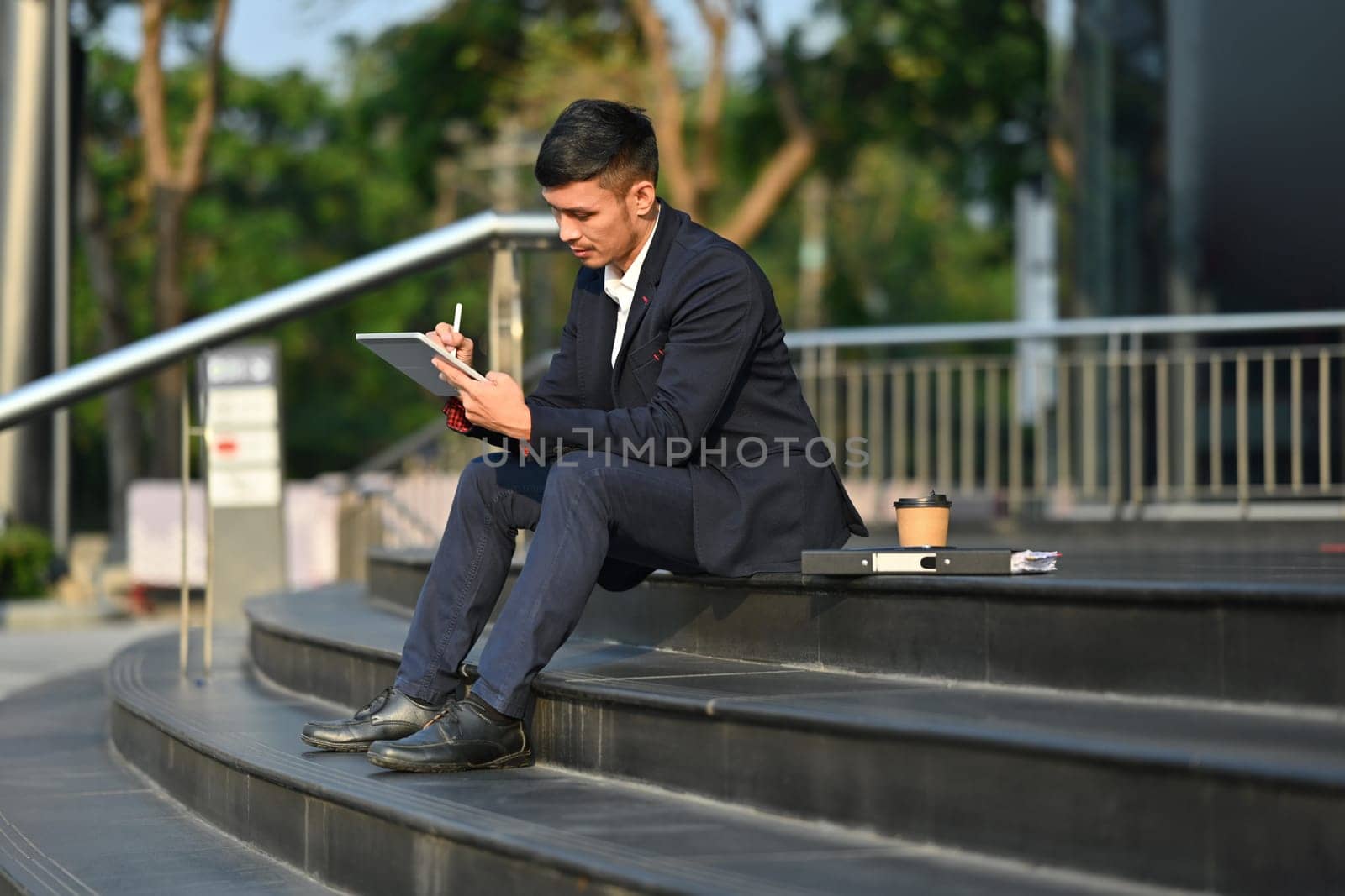 Full length of businessman in formalwear using digital tablet on stairs with in front of business center in early morning.
