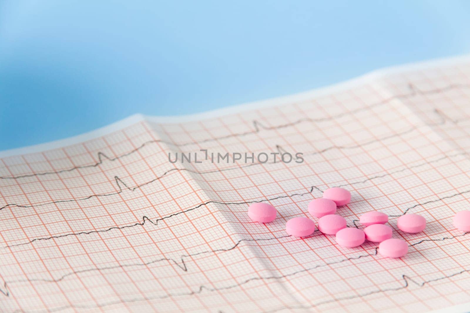 A large handful of pink pills lie on the electrocardiogram of the heart on a blue background. The concept of a healthy lifestyle and timely medical examination