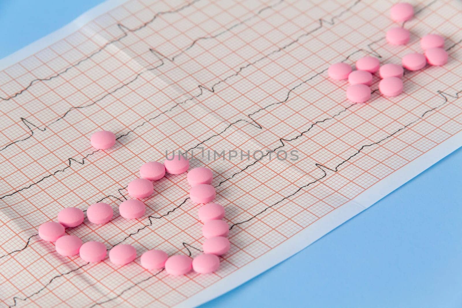 A large handful of pink pills lie in the form of a heart on an electrocardiogram, on a blue background. The concept of a healthy lifestyle and timely medical examination