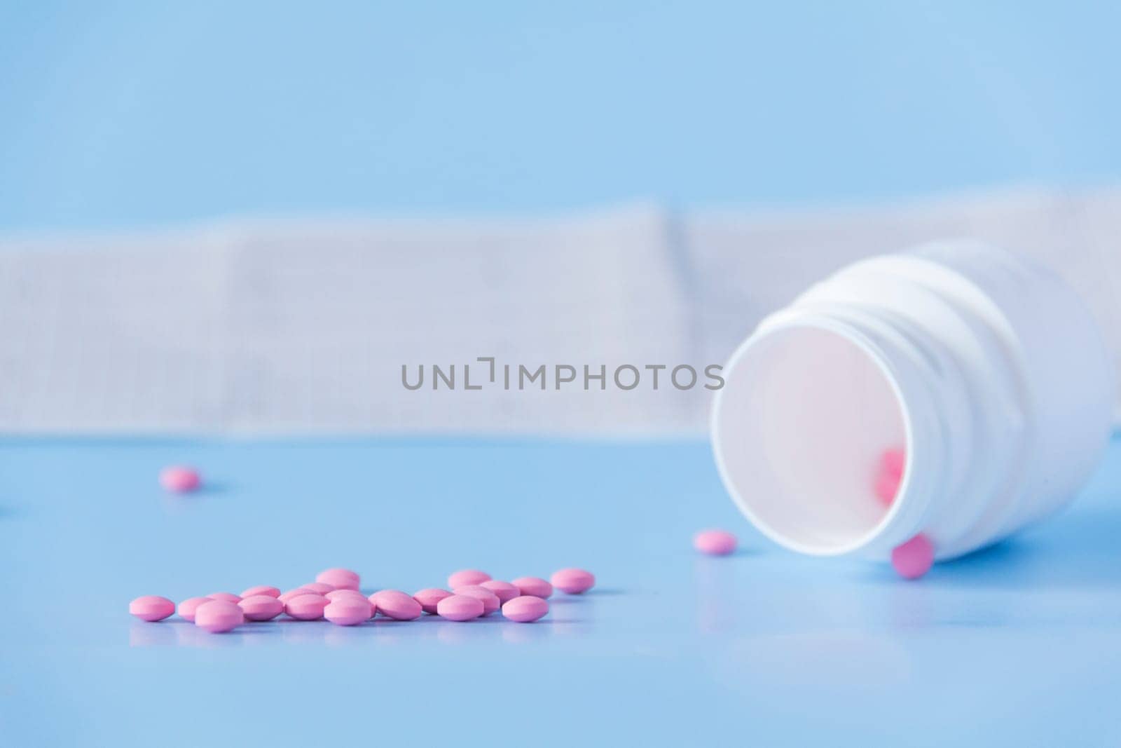 A large handful of pink pills poured out of a white jar on an electrocardiogram of the heart, on a blue background. The concept of a healthy lifestyle and timely medical examination. by Alla_Yurtayeva