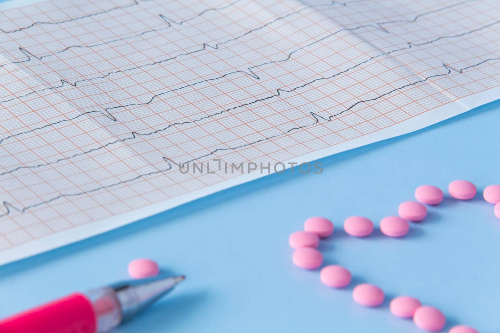 A large handful of pink pills lie in the form of a heart on an electrocardiogram, on a blue background. The concept of a healthy lifestyle and timely medical examination by Alla_Yurtayeva