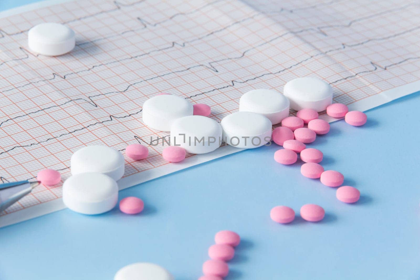 A large handful of pink and white medicines lie on the electrocardiogram of the heart, on a blue background. The concept of a healthy lifestyle and timely medical examination by Alla_Yurtayeva