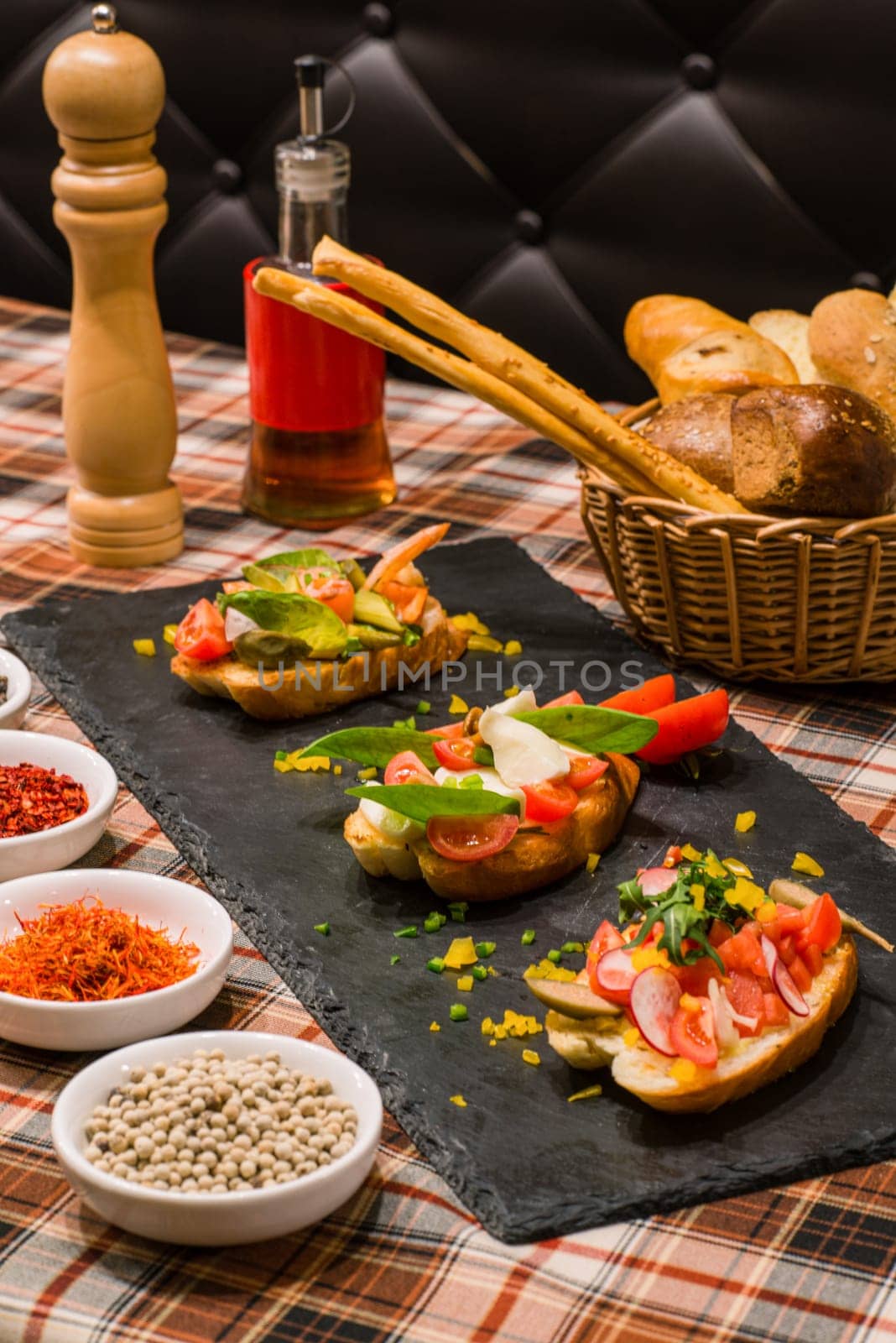 A closeup of serving table with tasty sandwiches or bruschetta with vegetables and spices on black board by A_Karim
