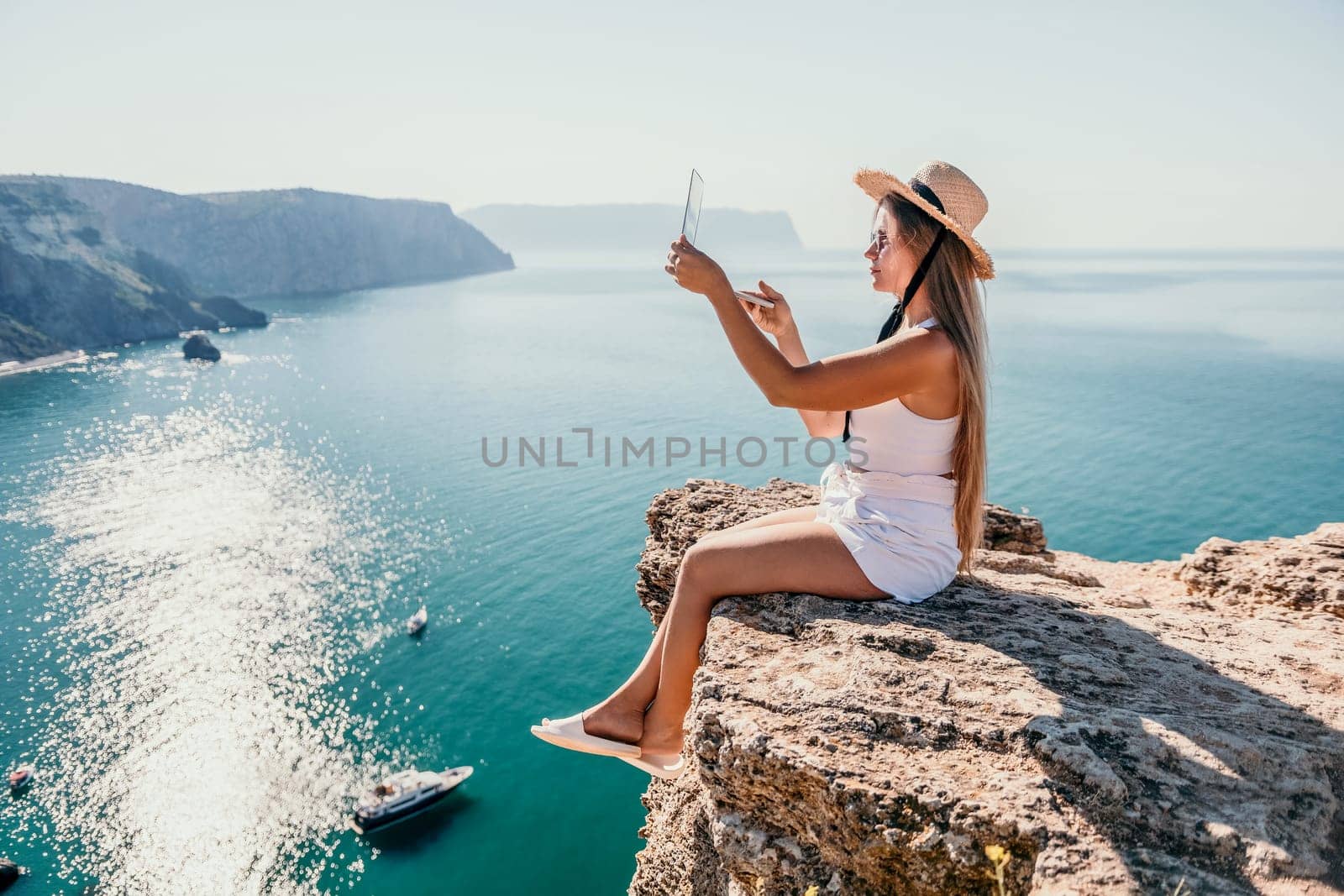 Woman laptop sea. Working remotely on seashore. Happy successful woman female freelancer in straw hat working on laptop by the sea at sunset. Freelance, remote work on vacation by panophotograph