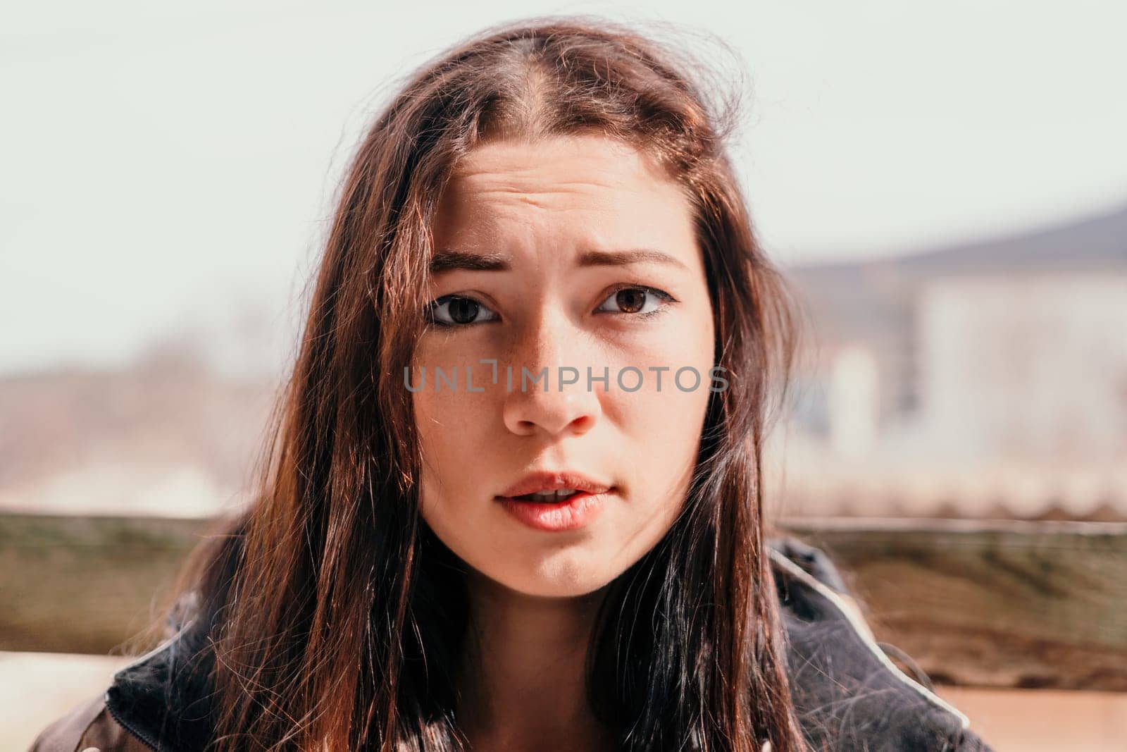 Happy young smiling woman with freckles outdoors portrait. Soft sunny colors. Outdoor close-up portrait of a young brunette woman and looking to the camera, posing against autumn nature background by panophotograph