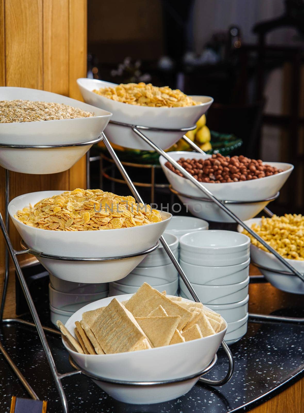 A vertical shot of a buffet table full of bowls with cornflakes, peanuts and cereal for breakfast by A_Karim