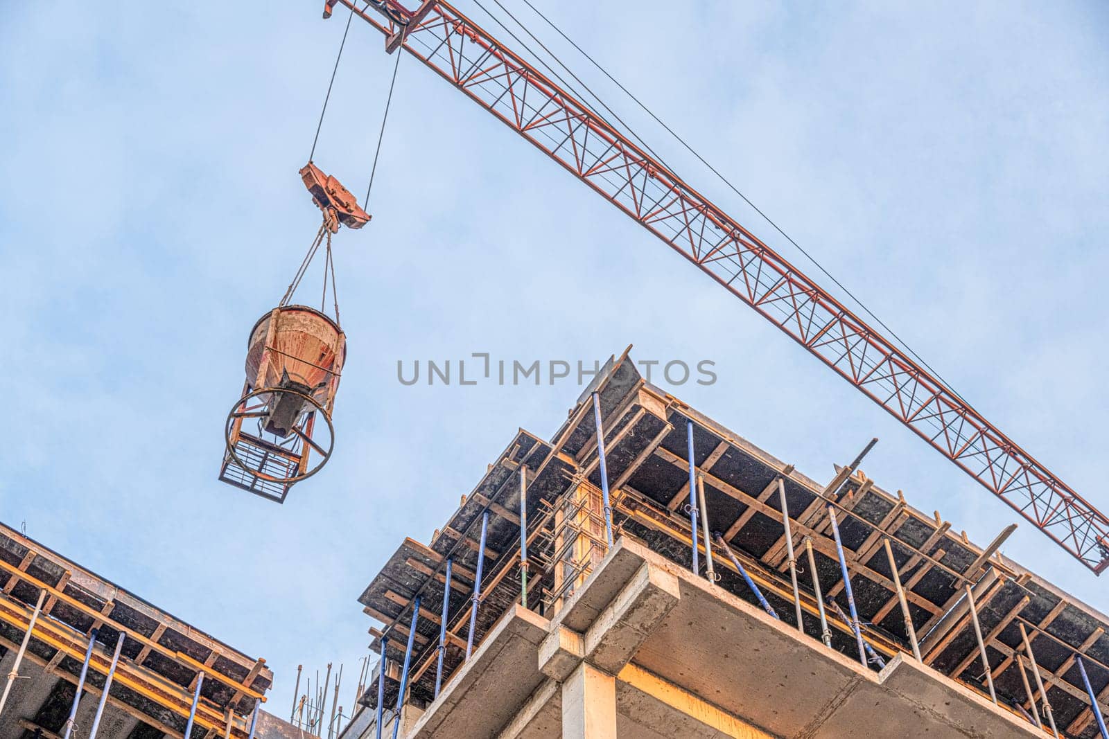 A low angle shot of a crane with equipment on a construction site with a new building infrastructure. Pouring concrete into a mold