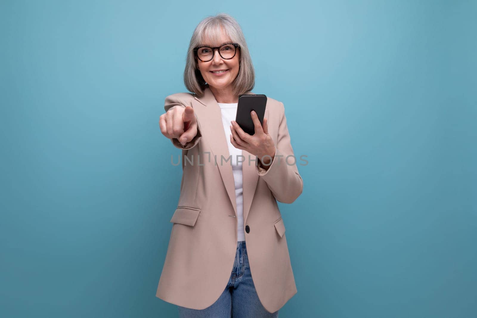 mature woman in a stylish image with a smartphone in her hands on a studio background with copy space.