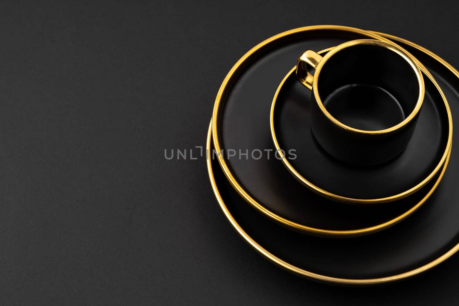 A set of black and golden ceramic plates and cup on a black background