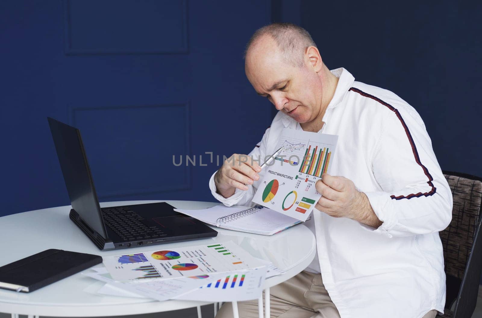 A man makes an online video call chat, sitting at home and talking into a laptop webcam, showing a document.