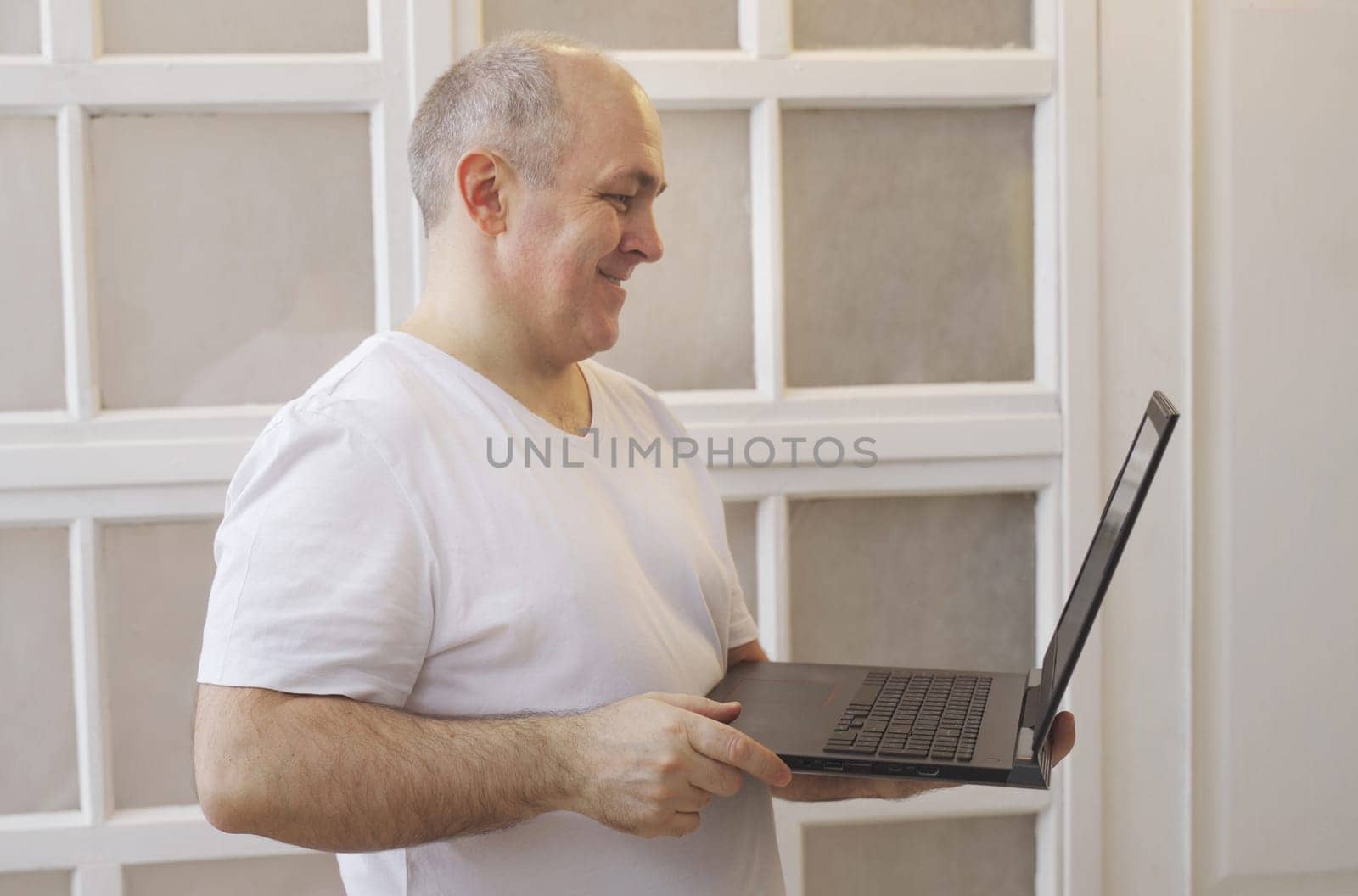 A man holds a laptop in his hands, stands at home and has a lively conversation on a video call.