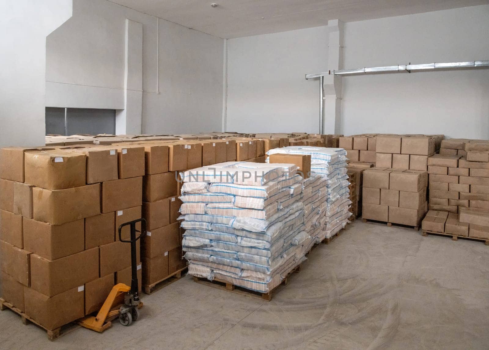 A pile of craft boxes and bags stacked on top of each other and a moving dolly in a white warehouse