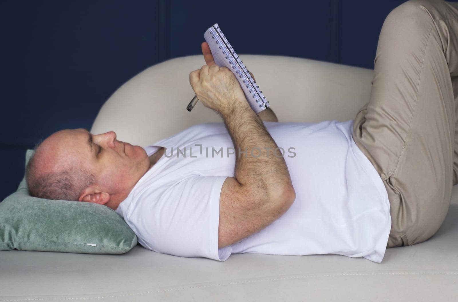 Young man lying on sofa and writing to do list in notepad