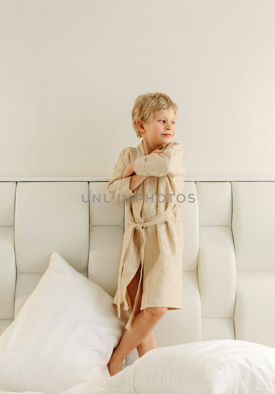 On the bed is a boy in a dressing gown with his arms crossed over his chest.