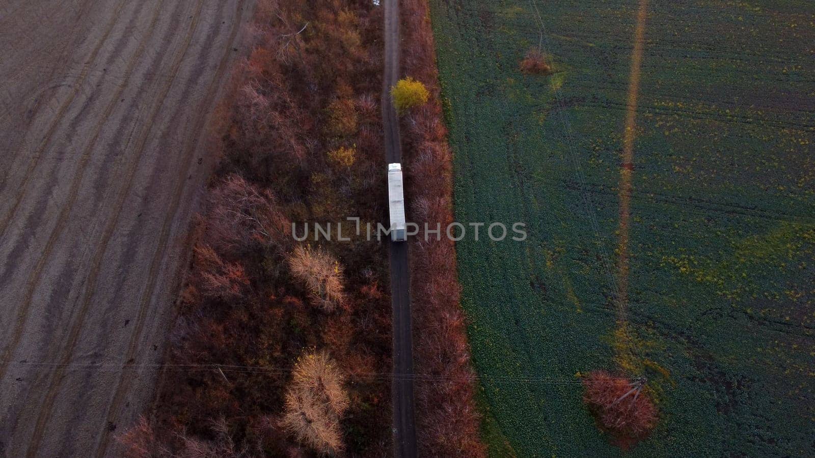 Large white cargo truck and white car driving dirt road between agricultural fields countryside. Top view, aerial drone view. Transport transportation delivery shipping, freight cargo transportation