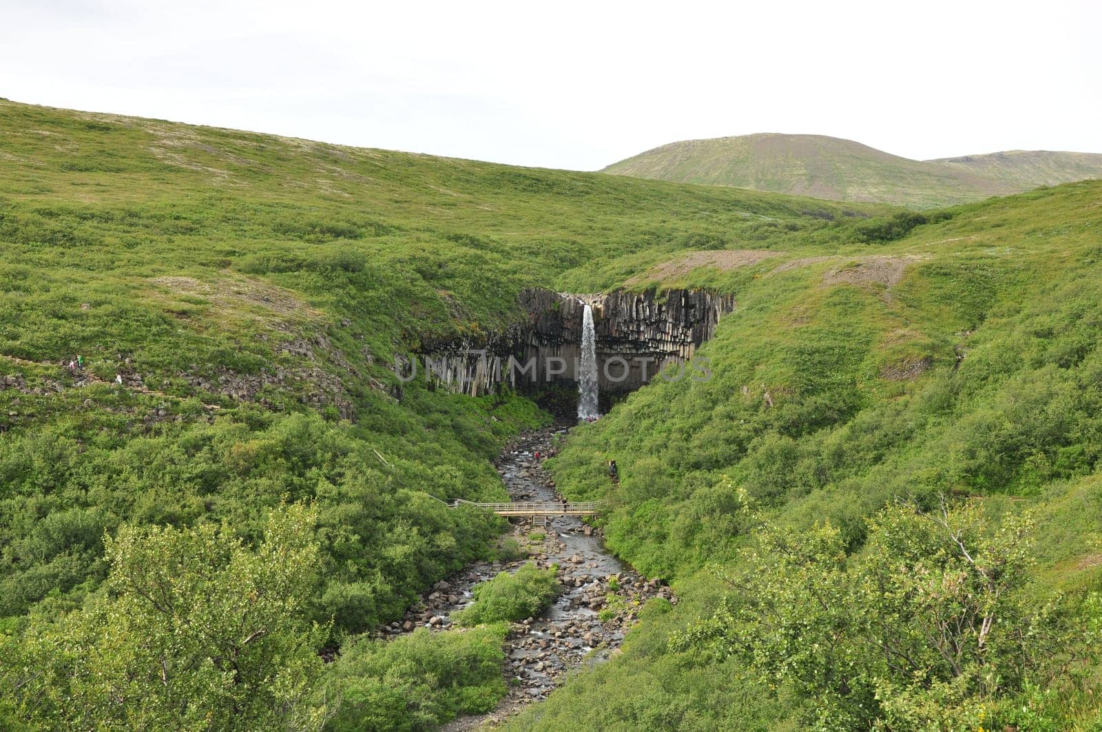 Scenic view of a waterfall flowing between grass cliffs under a gray sky