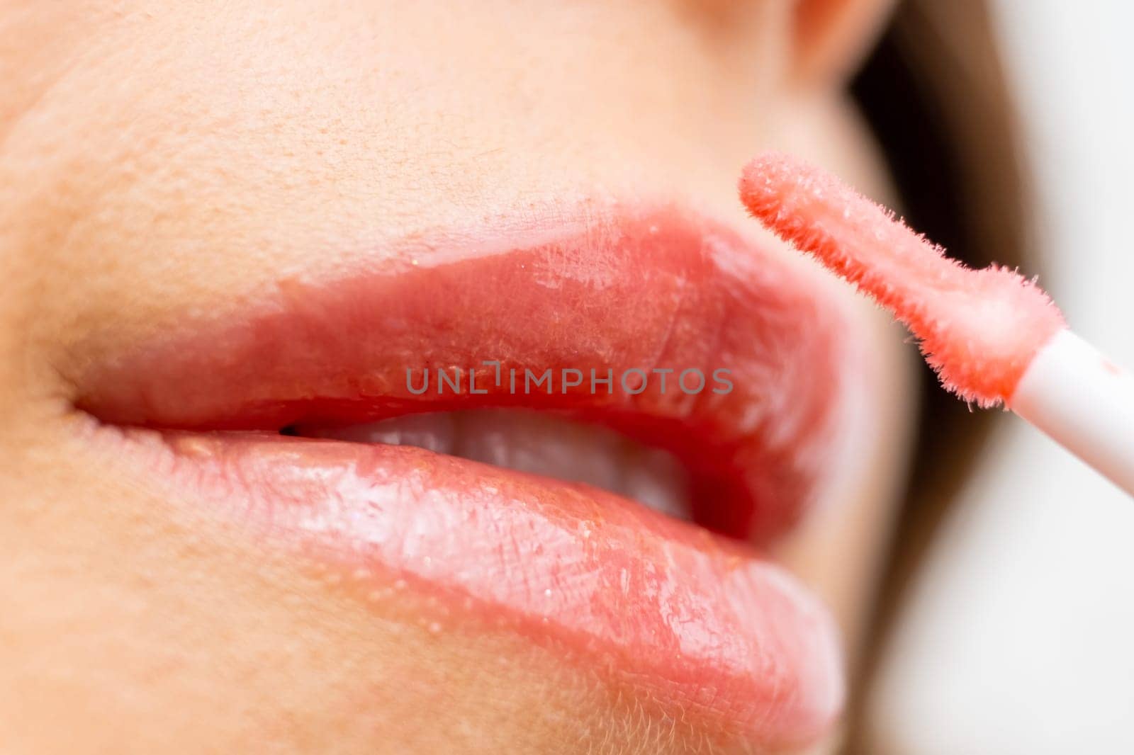 Charming young woman using a pink lip gloss and smile, close up.